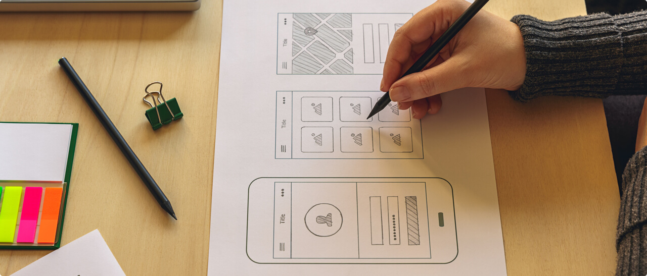 Person holding a pen drawing wireframes for an app
