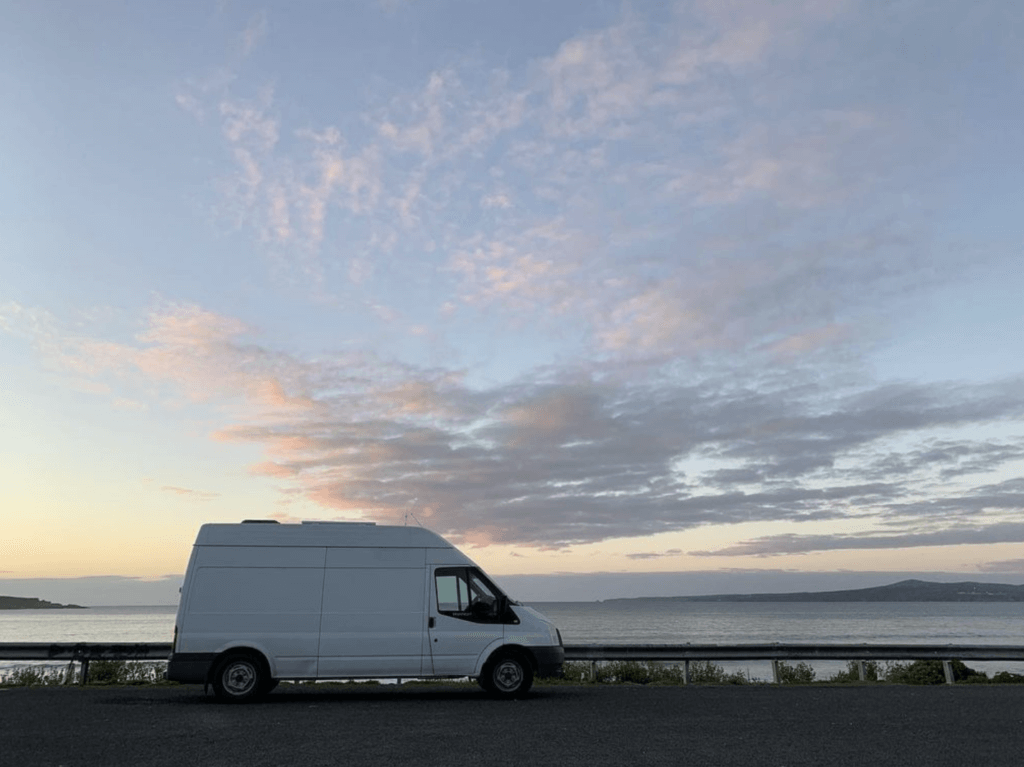 Photo of Simon Walduck's van where he has developed apps for startups and other clients, parked by the ocean in Eden NSW with a sweeping blue evening sky, sunset and pink clouds.