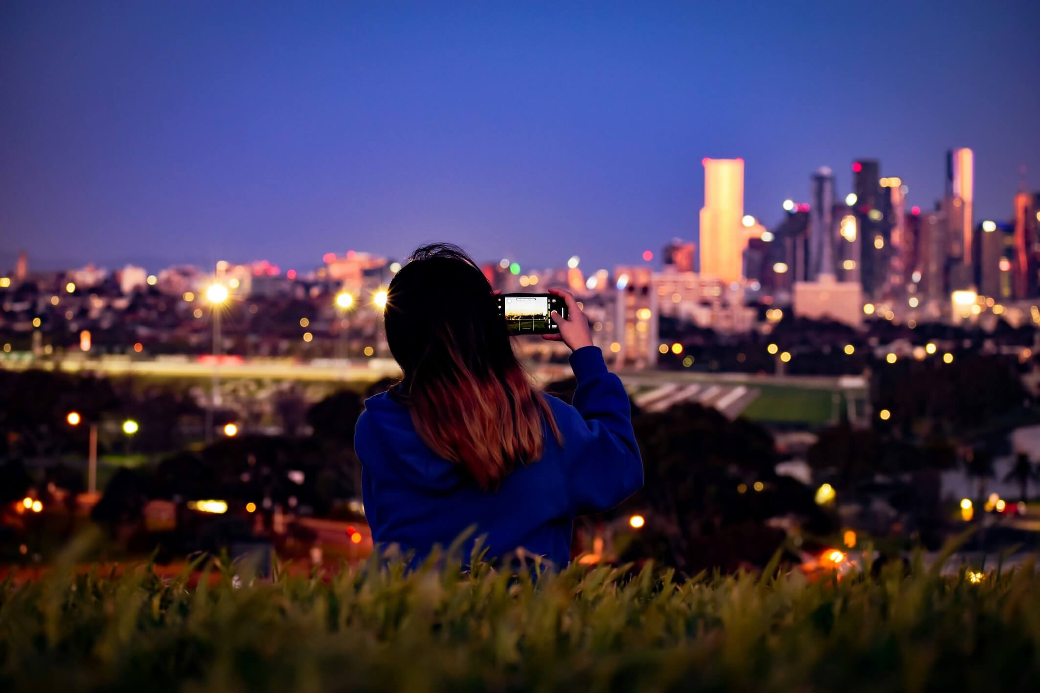 Person taking a photo of the city at night from a hilltop. To ensure your app success, ensure it can evolve with technology and user expectations. 